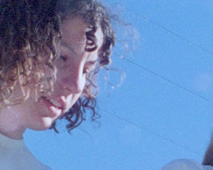 Filmstill aus Falling Out of Summer: Frau mit Locken vor blauem Himmel