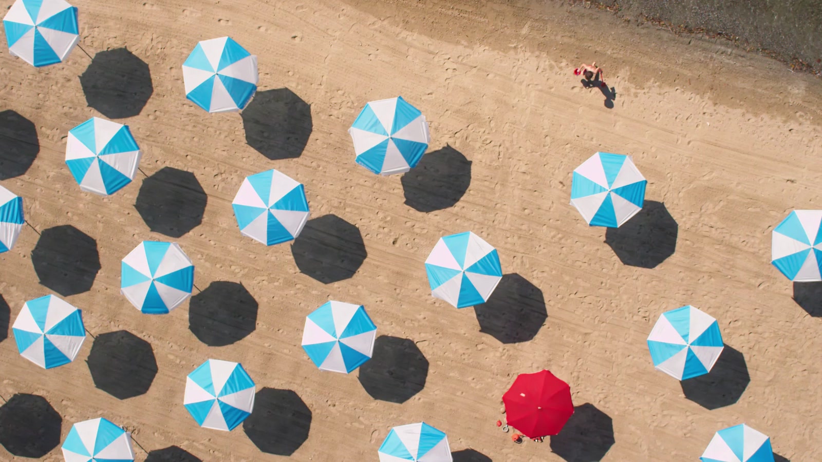 Filmstill aus UBS Summer Screens: blau-weisse Sonnenschirme und ein roter, von oben