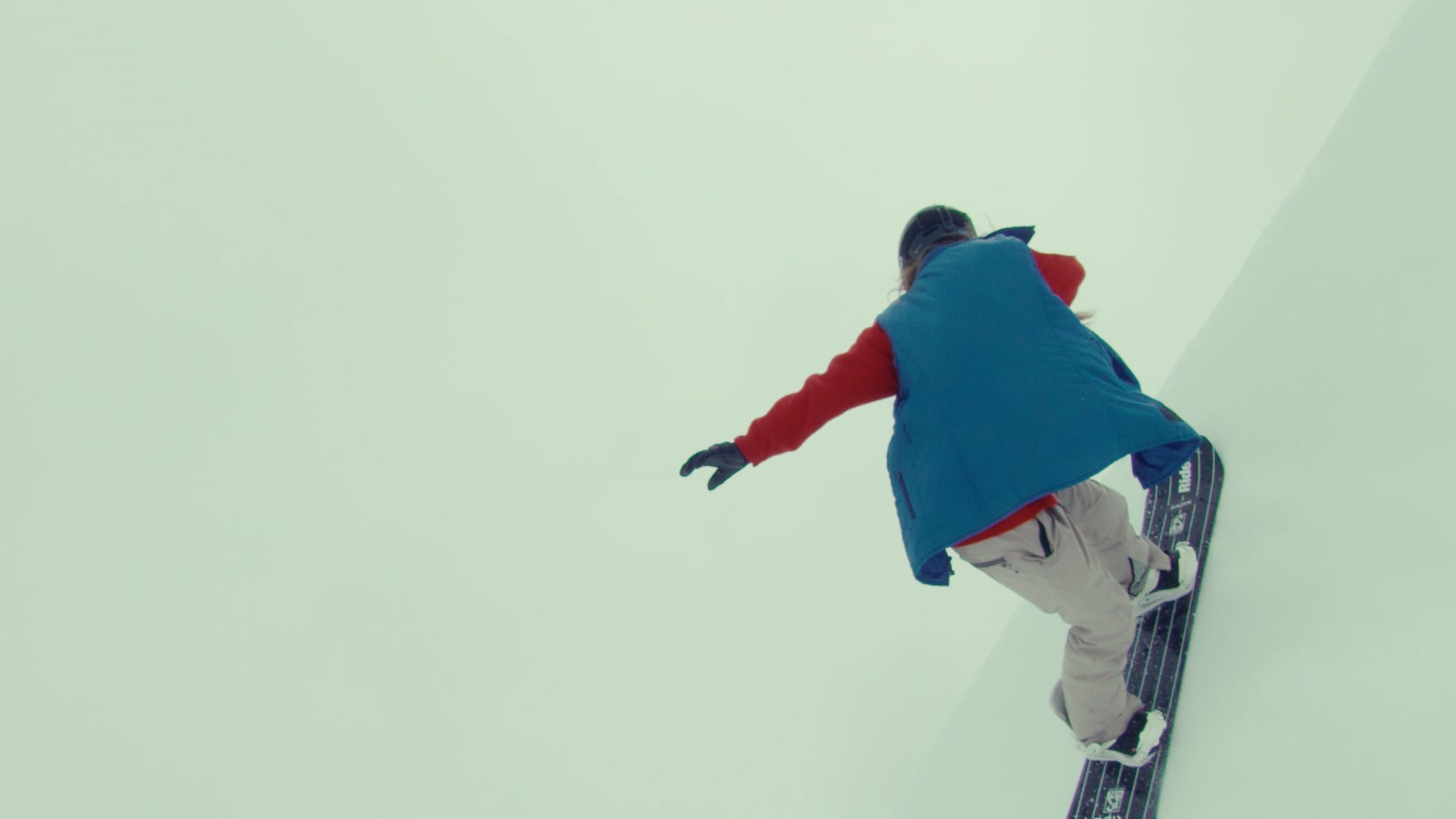 Filmstill aus Yet We Fly: Snowboarder in blauem Cape vor hellem Himmel, von unten
